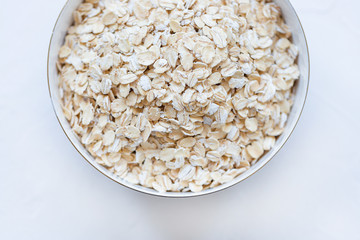 Oat flakes uncooked in a bowl on white background, concept of healthy eating vegan food Close up, selective focus, copy space