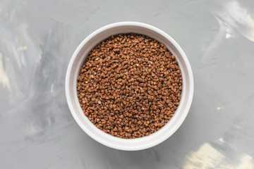 Raw buckwheat in ceramic bowl on gray background, concept of healthy eating vegan food. Close up, top view, selective focus, copy space