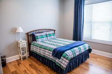 Light gray teenage boy bedroom with a wood bed and plaid bedspread and curtains in shades of blue,...