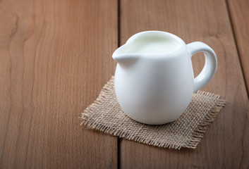 White jug with milk on a wooden rustic background.