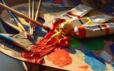 Paintbrushes, artist palette, oil paints on desk in painter studio.
