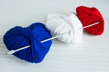 Three multicolored balls of wool in the shape of a heart: blue, red, white on a wooden table...