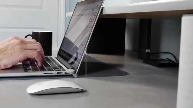Caucasian male working from home on MAC drinking coffee, closeup side view, slow motion