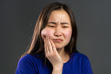 Young asian woman with tooth pain on grey studio background. Toothache, dental problems,...