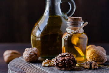 Concept of vegetable fat and oils for cooking and cosmetology. Glass bottle with essence, raw walnut peeled and in their shells. Wooden board, dark wooden background, close up, macro