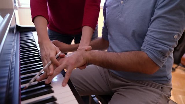 Female teacher giving a keyboard piano class to student. Correct hand position on keyboard. Detail of man practicing musical lessons indoors. House lifestyle learning music. Piano lessons at home.