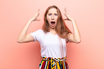 yound blonde woman screaming with hands up in the air, feeling furious, frustrated, stressed and...
