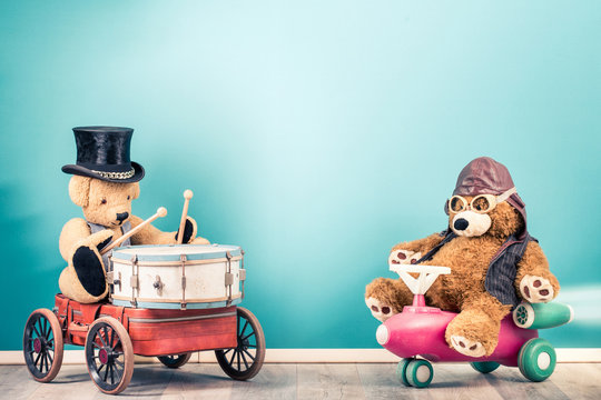 Retro Teddy Bear toy in cylinder hat playing classic drum on suitcase with wheels, Teddy Bear in leather aviator helmet and goggles on baby's shuttle front blue background. Vintage style photo