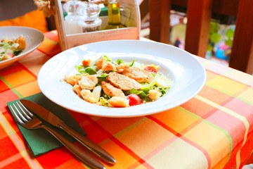 Caesar salad with croutons, quail eggs, cherry tomatoes and grilled chicken in a white plate on a table in a restaurant