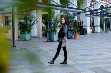 Fototapeta na wymiar Nice, brunette woman wearing in black leather jacket walking in square city. Smile, cute girl in Batumi, Georgia. Spring time.