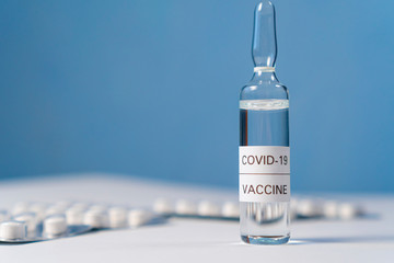 Coronavirus vaccine ampoule, from KOVID-19 on a white table with packs of white pills in a blister pack on a blue wall background. Copyspace. Close-up