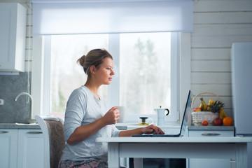 Woman with laptop and cup on the kitchen. Online shopping, work from home, freelance, online learning. Distance working concept