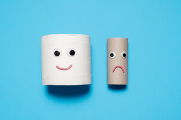 Happy smiling full toilet paper roll next to a sad and frowning empty toilet paper roll with googly eyes and mouth on a blue background with copy space and room for text 