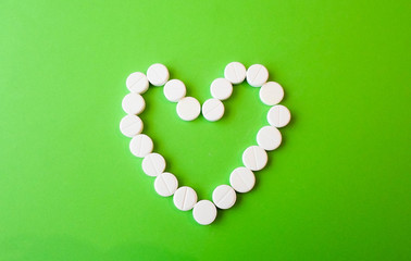 white pills on a green background in the shape of a heart. snow-white round antibiotics against viruses.