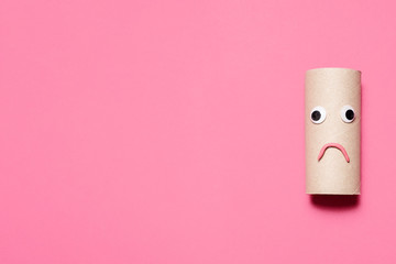 Sad frowning empty toilet paper roll with googly eyes and mouth on a pink background with room for...