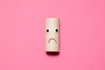Sad frowning empty toilet paper roll with googly eyes and mouth on a pink background with room for...
