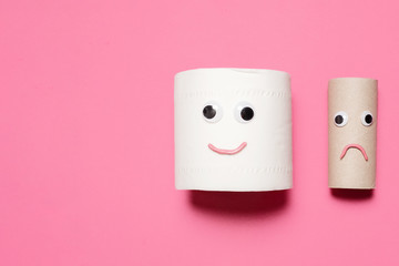 Happy smiling full toilet paper roll next to a sad and frowning empty toilet paper roll with googly eyes and mouth on a pink background with copy space and room for text with a right side composition