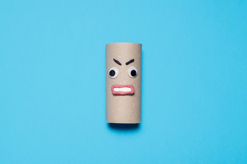 Angry empty toilet paper roll with googly eyes and mouth on a blue background with copy space and room for text
