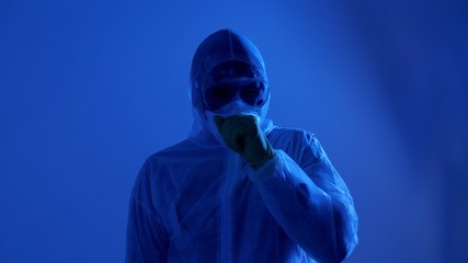 Man in protective medical mask, protective suit, coughs and sneezes. Coronavirus or COVID-19 prevention in dark.