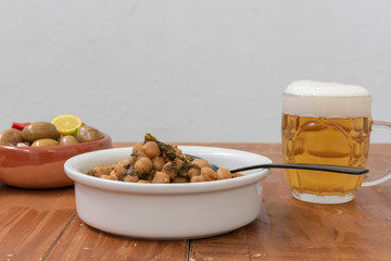Cuenco  de garbanzos con acelgas, una jarra de cerveza y aceitunas
