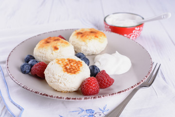 Tasty cheesecakes with sour cream and fresh blueberries at a plate and raspberries on white wooden table