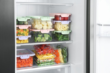 Plastic bags and containers with different frozen vegetables in refrigerator