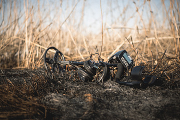 Professional metal detector on the burnt grass background.