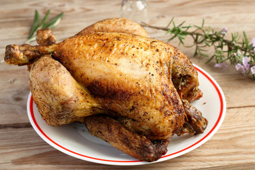 Pollo arrosto cotto allo spiedo su piatto bianco di ceramica e fondale di legno grezzo.