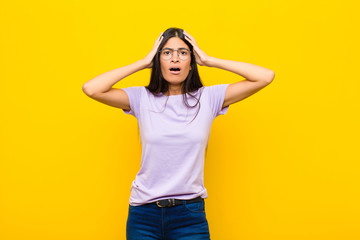 young pretty latin woman feeling horrified and shocked, raising hands to head and panicking at a...
