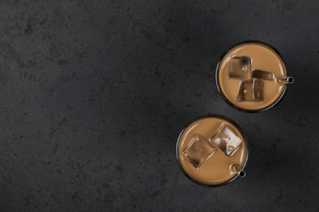 Coffee milk with ice in a glass with a metal tube on a dark background top view