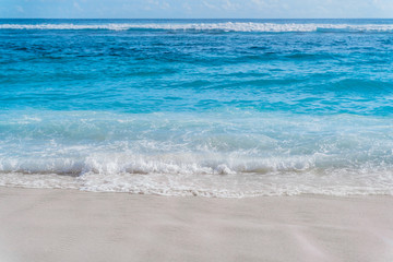 Fototapeta na wymiar Blue ocean water and yellow sand of Melasti beach in Bali. Waves roll on the sandy beach.