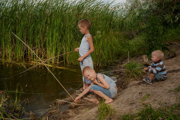 Funny children in colorful clothes took fishing rod and try to fish near river in the reeds. Funny situations while fishing. Summer vacation in village. Brothers are happy together