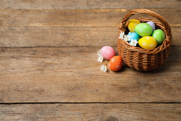 Colorful Easter eggs in basket and flowers on wooden background. Space for text