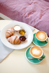 breakfast with cups of coffee with cream and croissants on wooden table