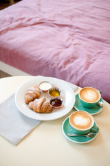 breakfast with cups of coffee with cream and croissants on wooden table
