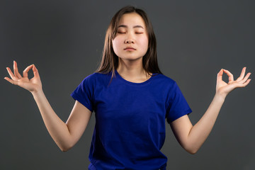Calm korean girl relaxing, meditating. Woman calms down, breathes deeply with mudra om on grey studio background
