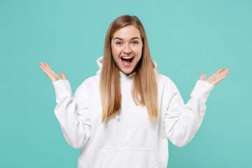 Excited young woman girl in casual white hoodie posing isolated on blue turquoise background studio portrait. People emotions lifestyle concept. Mock up copy space. Keeping mouth open spreading hands.