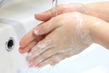 Children's soapy hands under running water under bathroom sink faucet