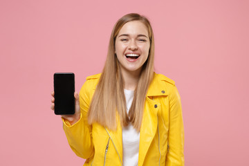 Fototapeta premium Laughing young woman girl in yellow leather jacket posing isolated on pastel pink background studio portrait. People lifestyle concept. Mock up copy space. Hold mobile phone with blank empty screen.