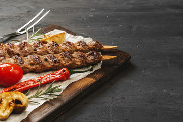 Grilled Lula kebab on skewers served on wooden board, black table background