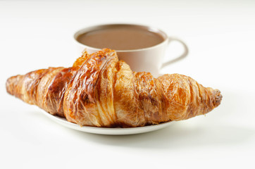 Delicious croissant on a ceramic saucer with coffee in a cup