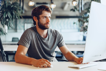 Fototapeta na wymiar Bearded man freelancer using computer in a modern coworking place. Freelance business concept