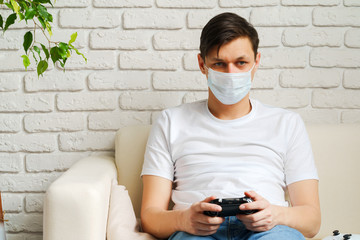 Young white man playing video games with medical mask on his face while Covid-19 quarantine