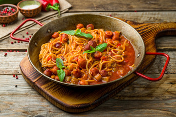 Spaghetti with sausage in tomato sauce on old wooden table