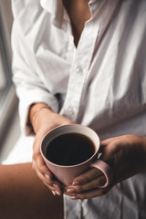 Woman in a white t-shirt holds morning coffee in a pink ceramic cup. Manicure. Front view