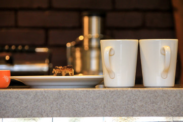 two white cups and a plate with cakes on the table, side view