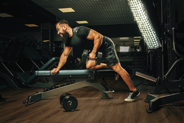 Fototapeta na wymiar Muscular young man lifting weights in a dark gym