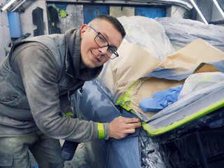 cheerful, young man with glasses polishes, primes and paints a car in the garage