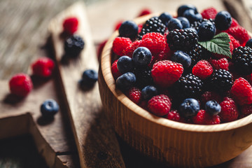 blueberries and raspberries, blackberry in a wooden bowl on old wood background