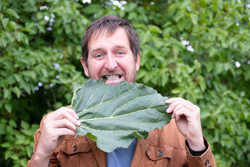 a bearded man eats a leaf of green burdock outside